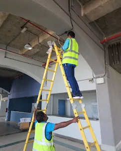 IP Care technicians installing a soffit-mounted CCTV camera from a ladder at Al Jeel Tower, Abu Dhabi